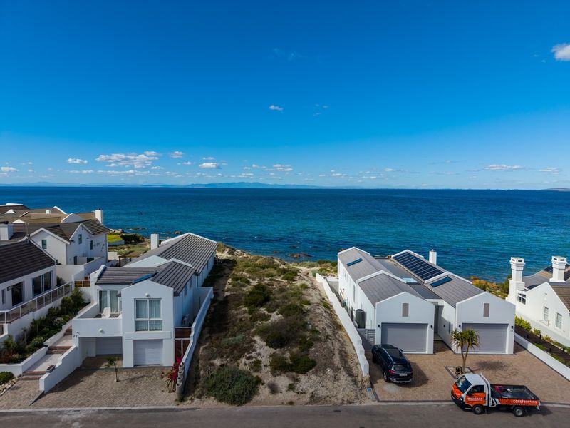 Aerial view of residential properties situated along the coastline, featuring paved driveways, solar panels, and direct ocean views.