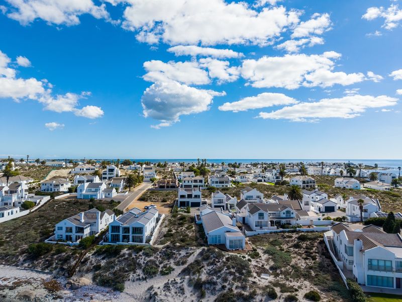 An aerial view of a coastal residential estate featuring multiple homes, paved streets, and natural sand dune landscaping overlooking the ocean.