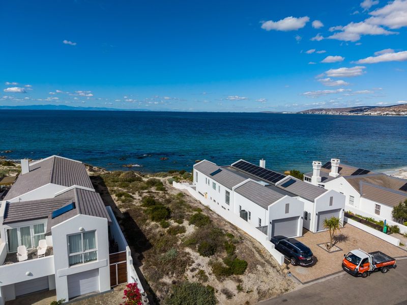 Aerial view of coastal residential properties featuring modern architecture, solar panels, and direct proximity to the ocean.