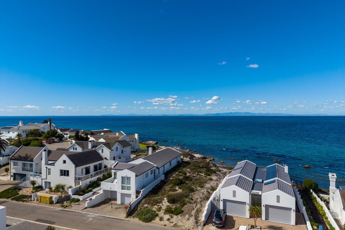 Aerial view of a coastal residential estate featuring modern homes with pitched roofs, solar panels, and direct proximity to the ocean.