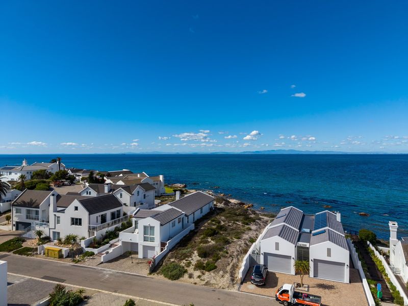 Aerial view of a coastal residential estate featuring modern homes with pitched roofs, solar panels, and direct proximity to the ocean.