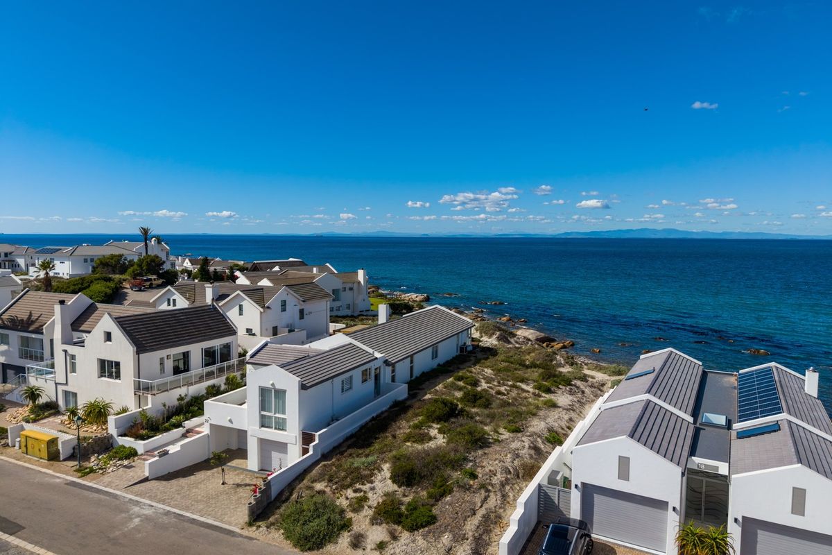 Aerial view of a coastal residential estate featuring modern homes with tiled roofs, solar panels, and direct proximity to the ocean.