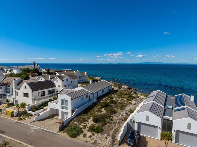 Aerial view of a coastal residential estate featuring modern homes with tiled roofs, solar panels, and direct proximity to the ocean.