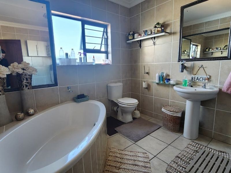 A well-maintained bathroom featuring a freestanding bathtub, pedestal basin, toilet, and neutral floor-to-ceiling wall tiles with a functional window for natural light.