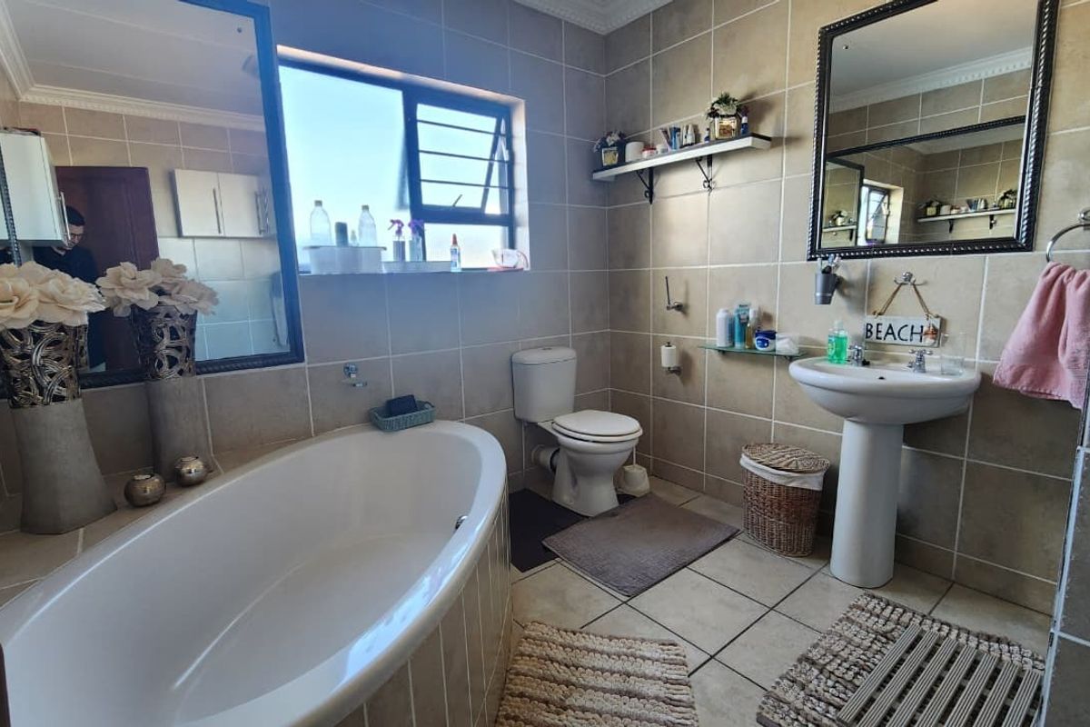 A well-maintained bathroom featuring a freestanding bathtub, pedestal basin, toilet, and neutral floor-to-ceiling wall tiles with a functional window for natural light.