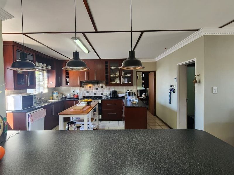 A functional kitchen featuring dark wood cabinetry, granite countertops, tiled backsplash, and modern pendant lighting, offering a practical layout for cooking and meal preparation.