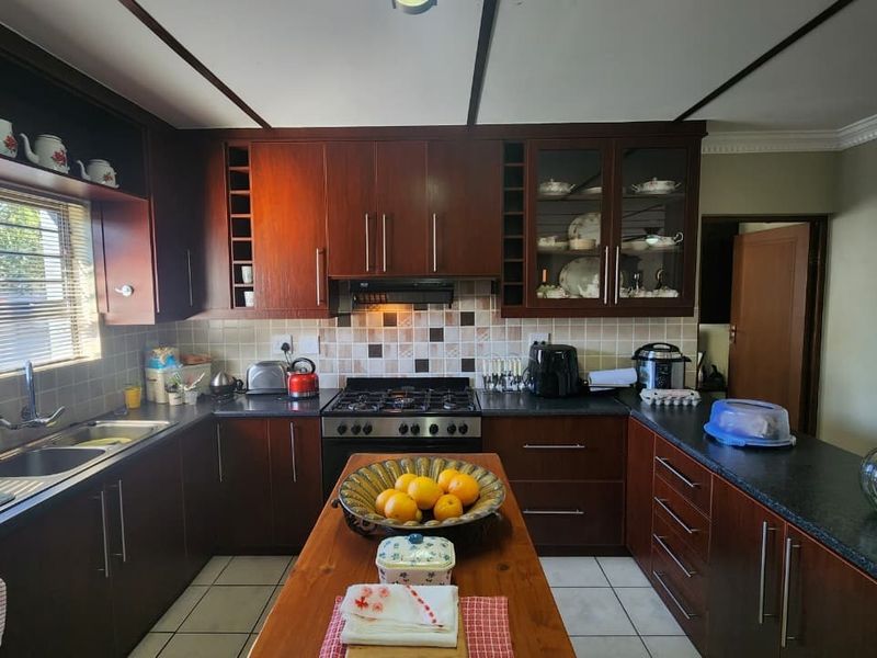 A functional kitchen featuring dark wood cabinetry, a central island, gas hob, extractor fan, and tiled backsplash with ample counter space.