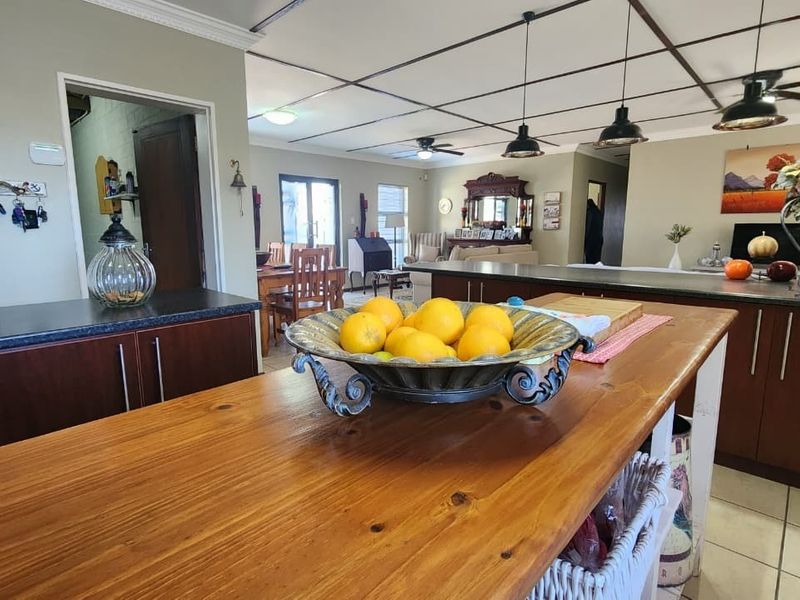 Spacious open-plan kitchen and living area featuring a wooden kitchen island, dark cabinetry, tiled floors, and modern pendant lighting.