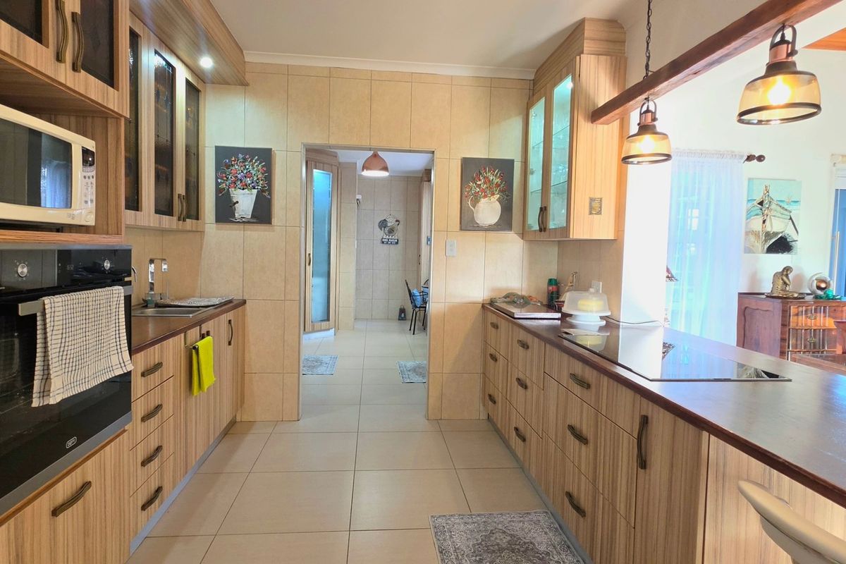A well-maintained kitchen featuring wood-finish cabinetry, built-in appliances, a breakfast bar, and tiled flooring, leading through to an adjacent living area.