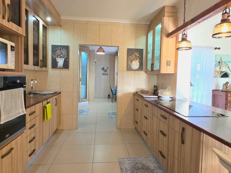 A well-maintained kitchen featuring wood-finish cabinetry, built-in appliances, a breakfast bar, and tiled flooring, leading through to an adjacent living area.