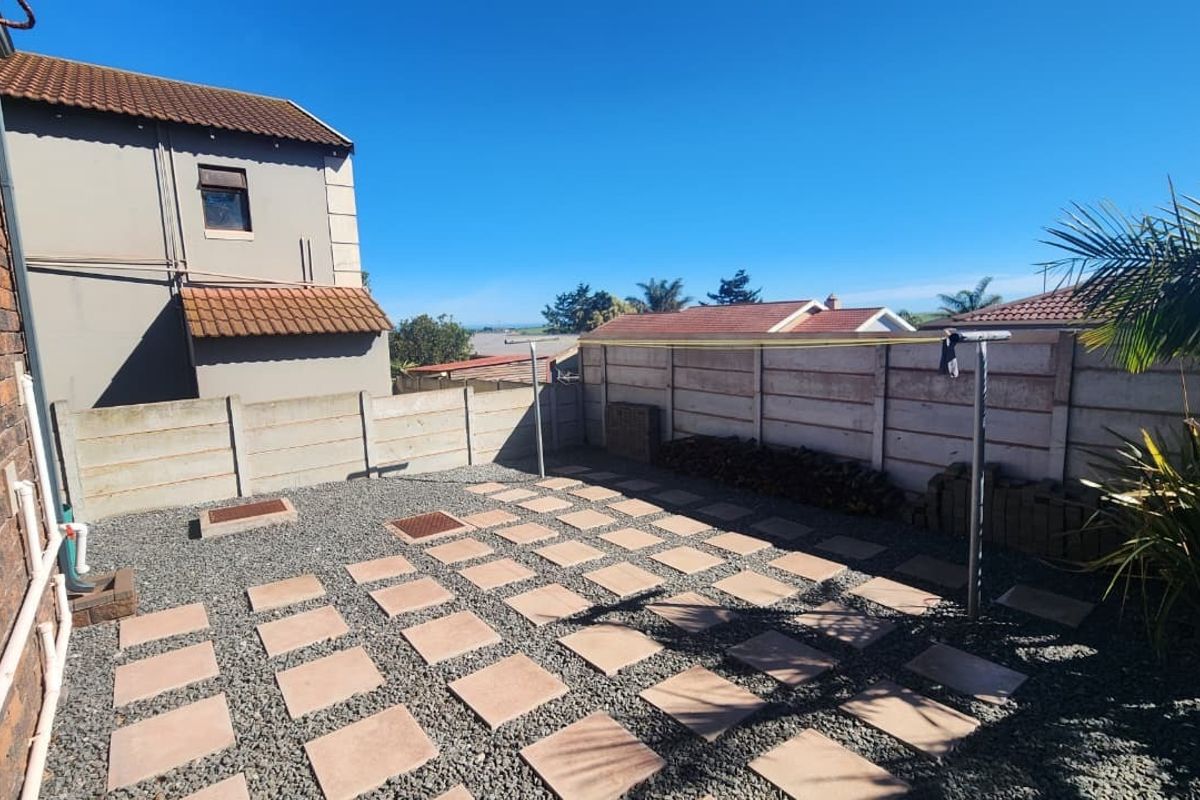 A low-maintenance rear courtyard featuring a paved patio area, gravel landscaping, and secure precast concrete boundary walls.