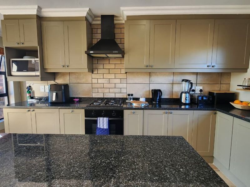 A well-maintained kitchen featuring granite countertops, a central island, built-in cabinetry, and a gas hob with a modern extractor fan.