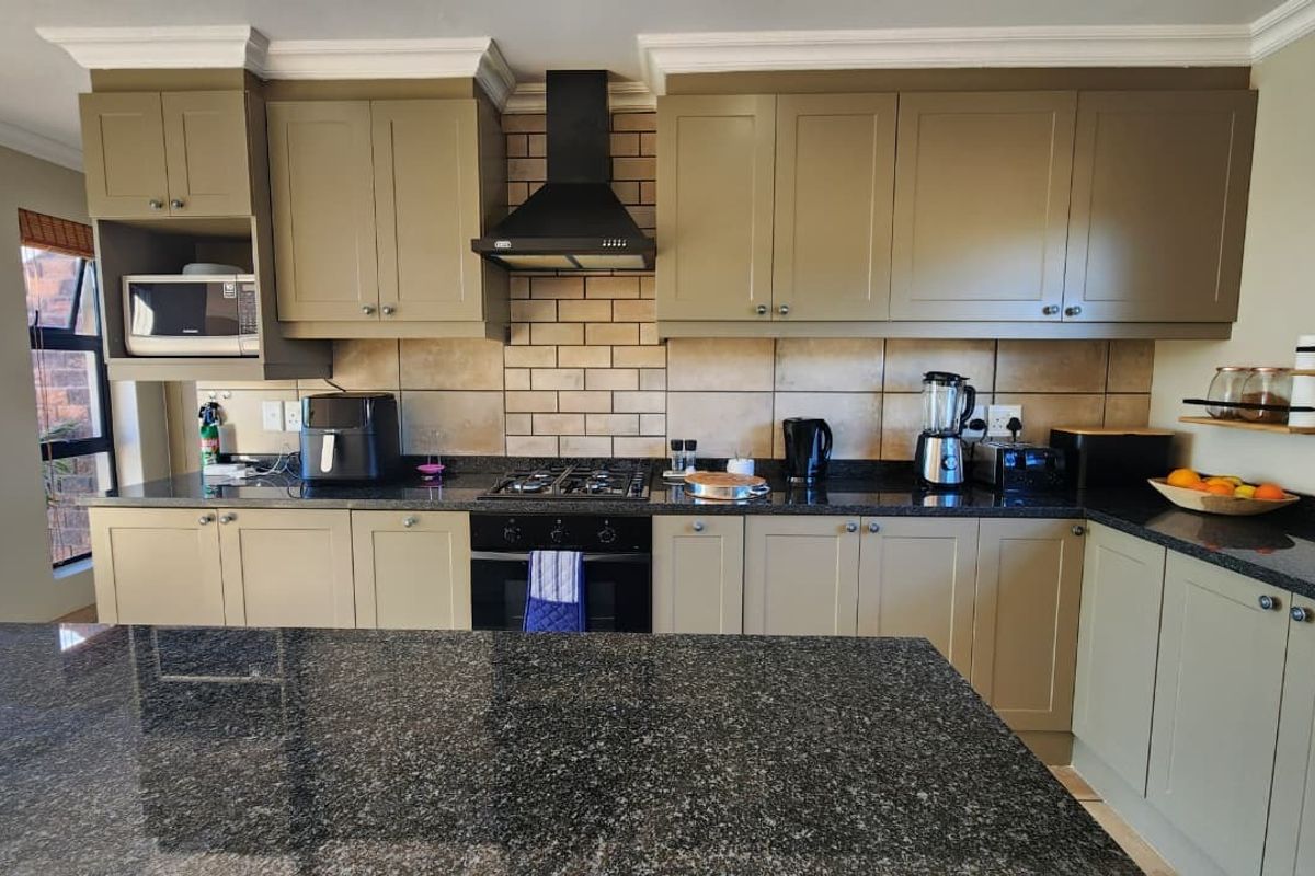A well-maintained kitchen featuring granite countertops, a central island, built-in cabinetry, and a gas hob with a modern extractor fan.
