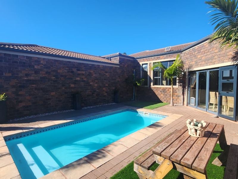 A well-maintained outdoor pool area featuring a paved patio, artificial turf, and direct access to the home through folding glass doors.