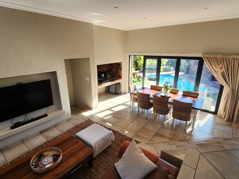 Spacious open-plan living and dining area featuring a built-in television recess, indoor braai, and large sliding doors opening to the pool area.