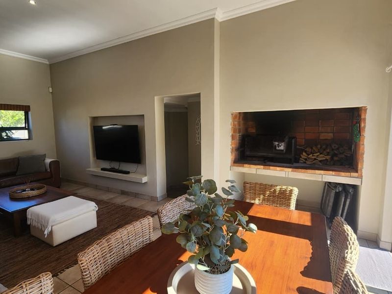 Spacious open-plan living and dining area featuring a built-in brick braai, recessed TV niche, and large sliding doors leading to the outdoor space.