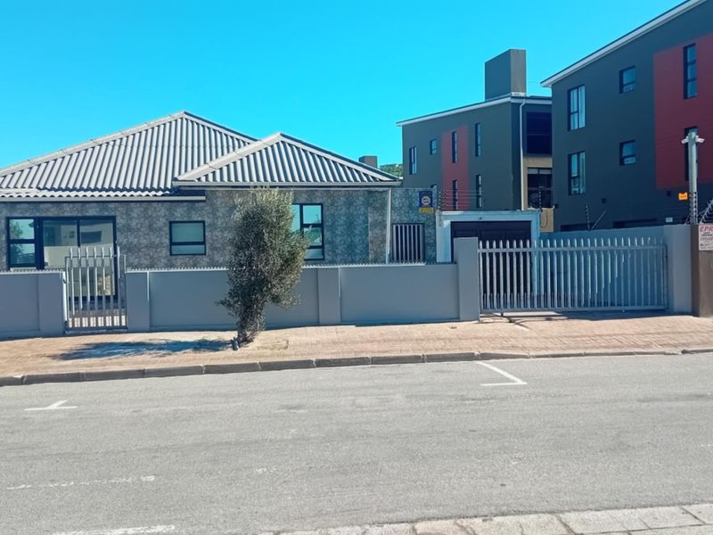 Front elevation of a residential property featuring a tiled roof, secure perimeter wall with electric fencing, and a paved driveway entrance.