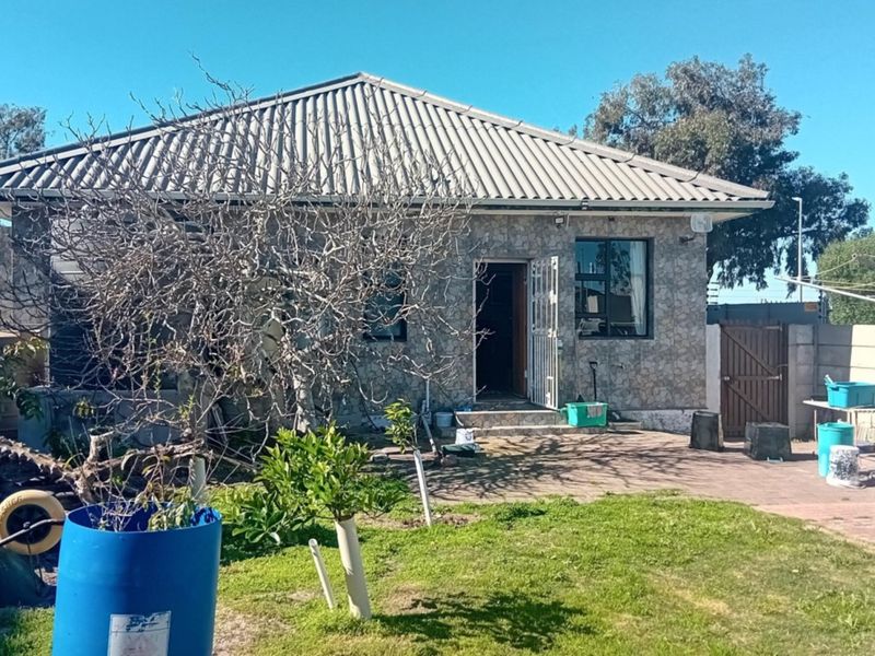 Rear view of a single-story house featuring stone cladding, a tiled roof, and a paved patio area leading into the garden.