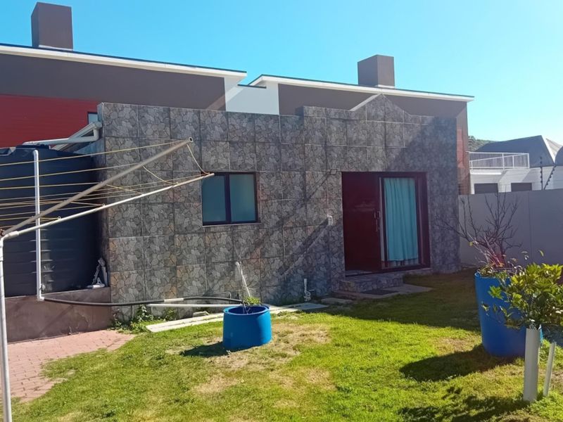 Rear view of the property featuring a stone-clad facade, sliding glass door access, and a private garden area with a water storage tank.