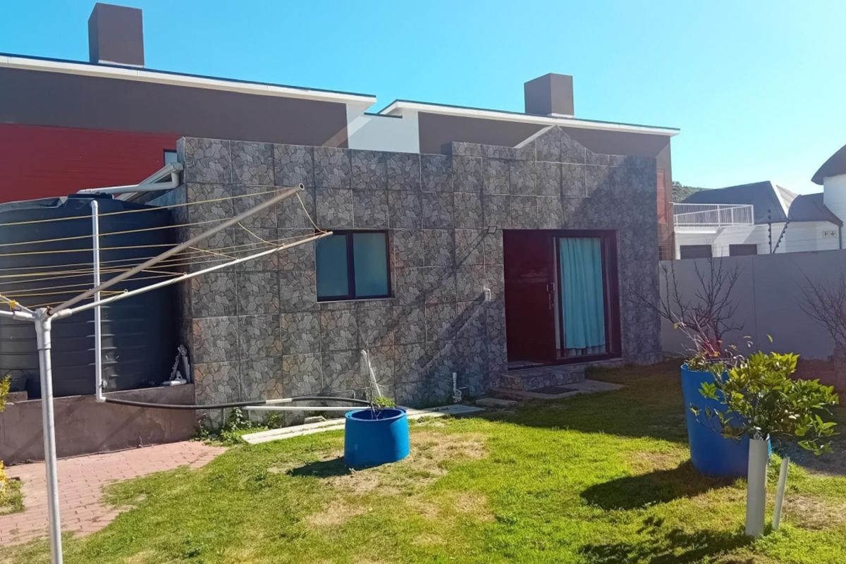 Rear view of the property featuring a stone-clad facade, sliding glass door access, and a private garden area with a water storage tank.