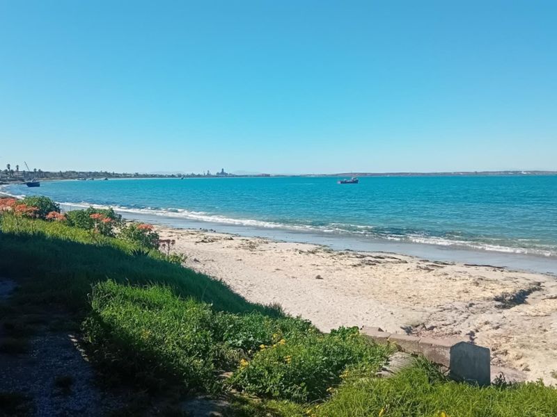 A scenic view of the coastline featuring a sandy beach and clear blue ocean waters.