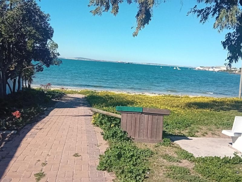 A scenic view of the coastline featuring a paved walkway leading towards the beach and ocean.