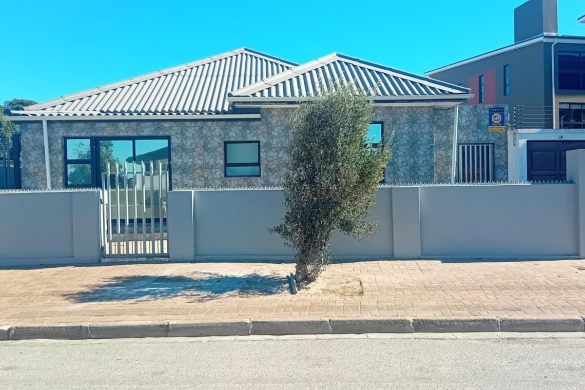 Front elevation of a single-story house featuring stone cladding, a tiled roof, and a secure perimeter wall with metal gate access.