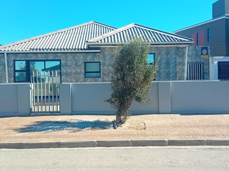 Front elevation of a single-story house featuring stone cladding, a tiled roof, and a secure perimeter wall with metal gate access.
