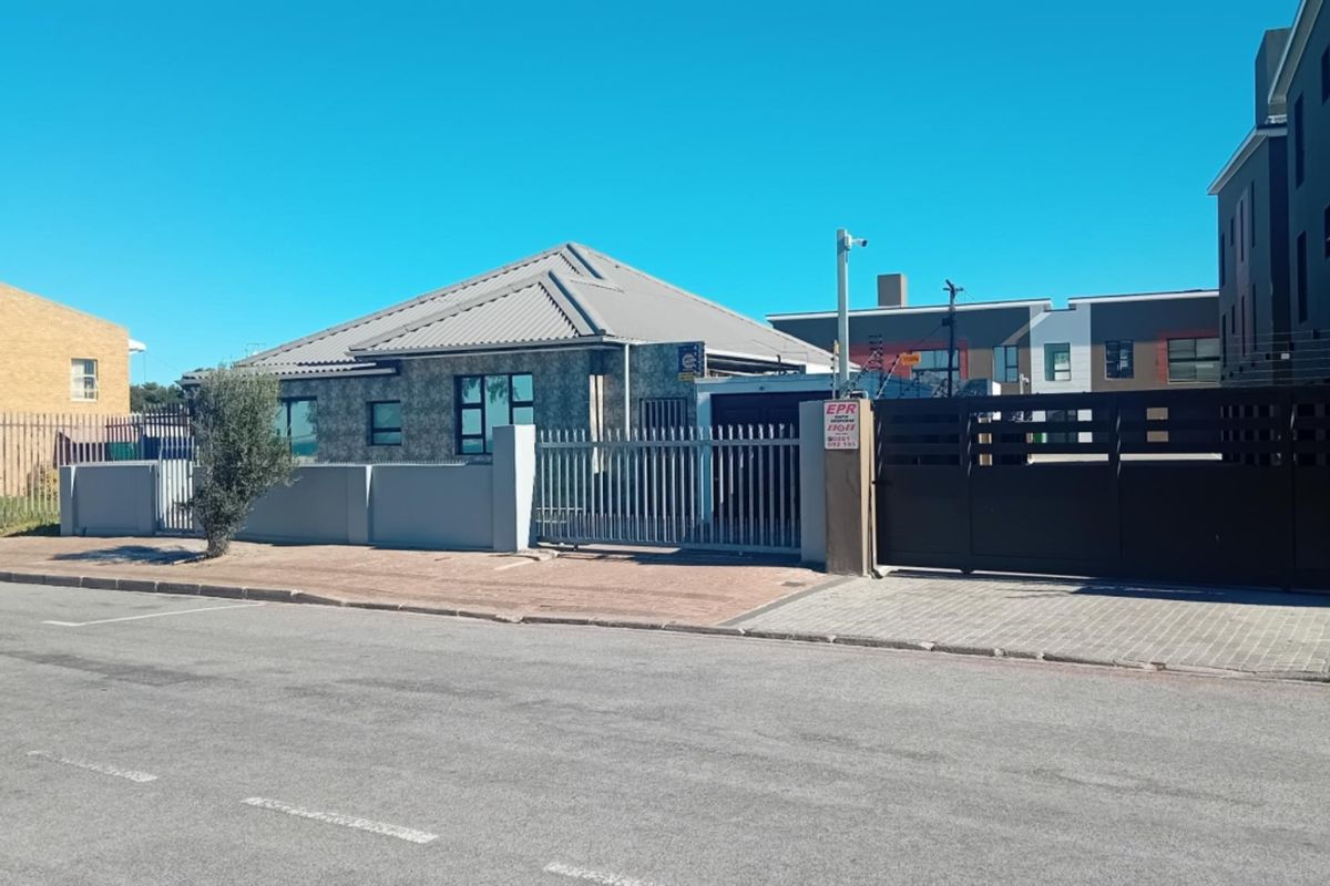 Front exterior view of the property featuring a metal roof, paved driveway, secure perimeter wall with electric fencing, and gated access.