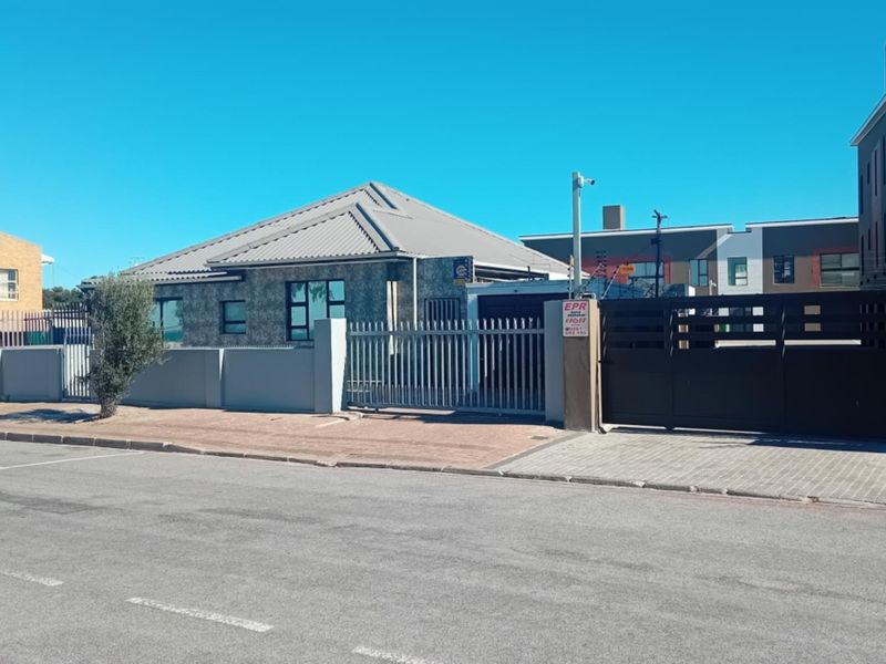 Front exterior view of the property featuring a metal roof, paved driveway, secure perimeter wall with electric fencing, and gated access.