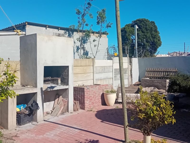 Rear outdoor area featuring a built-in braai, brick paving, and perimeter precast concrete walling, offering potential for landscaping and entertainment space development.