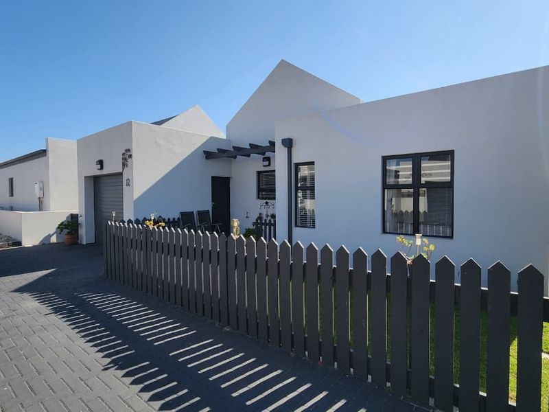 Modern single-story house exterior featuring a clean white facade, dark aluminium window frames, a timber pergola, and a neat picket fence with paved driveway.