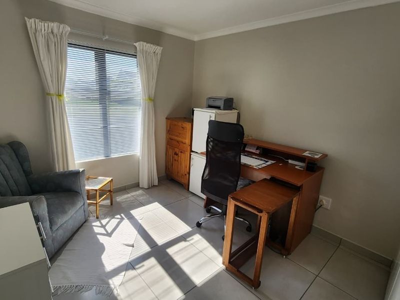 A functional home office space featuring neutral wall tones, tiled flooring, and a window with fitted blinds, providing a bright and practical workspace.