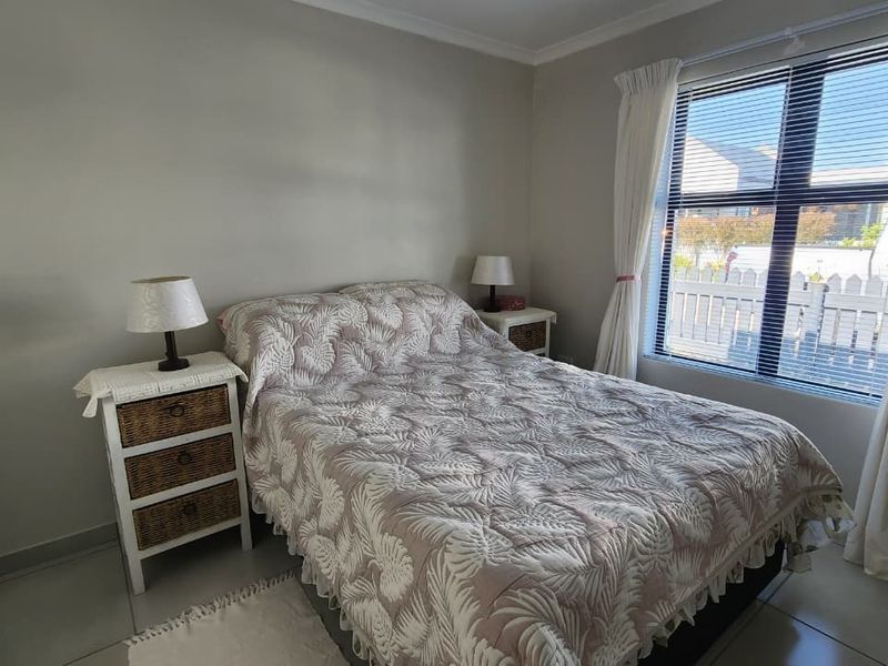 A well-lit bedroom featuring neutral tiled flooring, a large window with venetian blinds, and coved ceiling detailing.