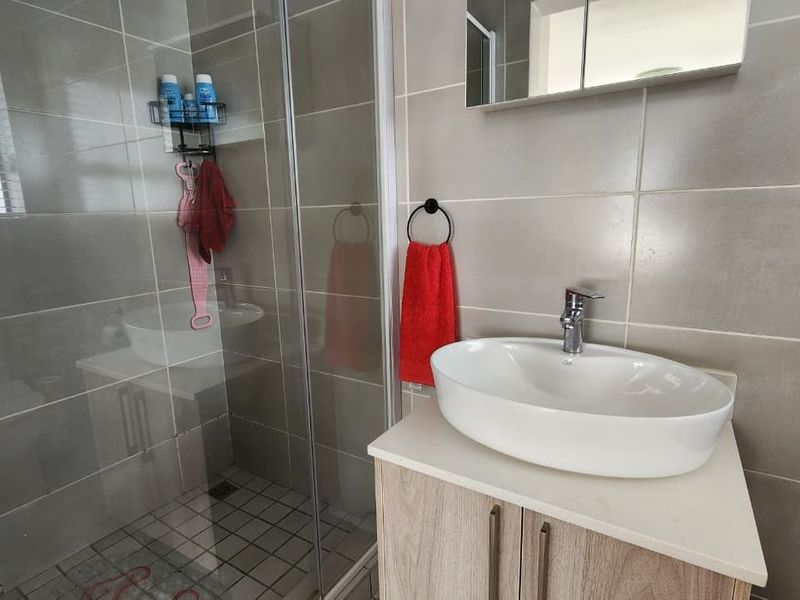 Modern bathroom featuring a glass shower enclosure, a contemporary vessel sink with vanity cabinet, and neutral wall tiling.