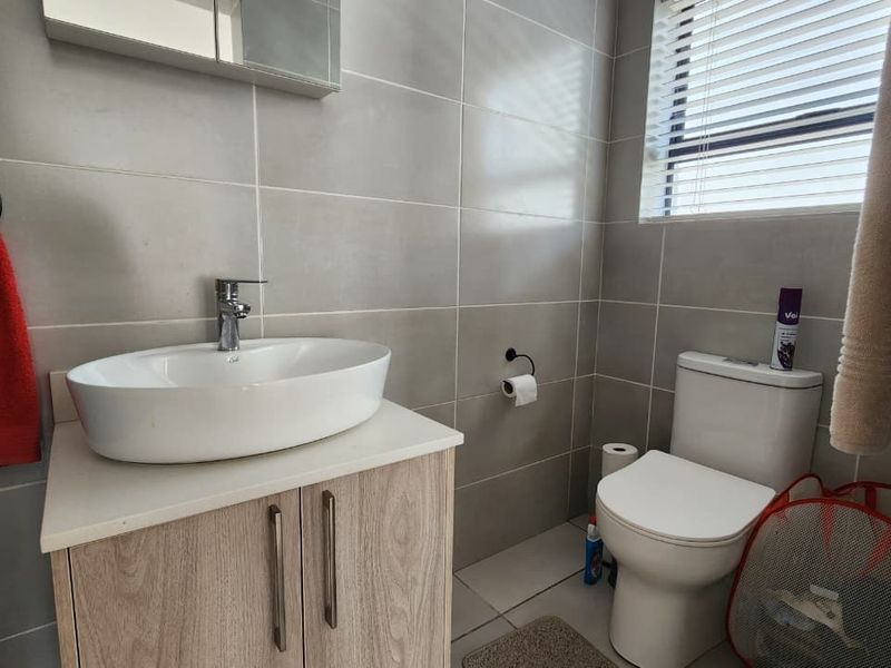 A modern bathroom featuring a vessel sink on a wood-finish vanity, tiled walls, and a standard toilet with venetian blinds.