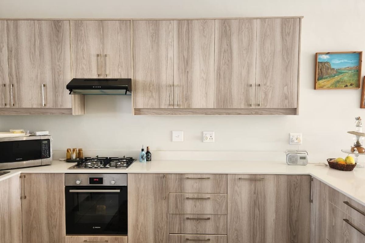 Modern kitchen featuring light wood-grain cabinetry, stone countertops, a built-in gas hob, oven, and extractor fan.