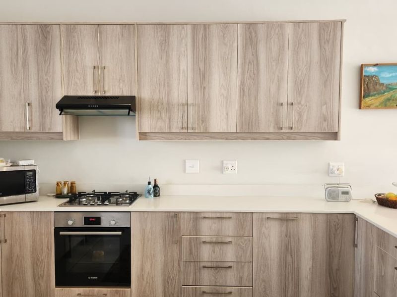 Modern kitchen featuring light wood-grain cabinetry, stone countertops, a built-in gas hob, oven, and extractor fan.