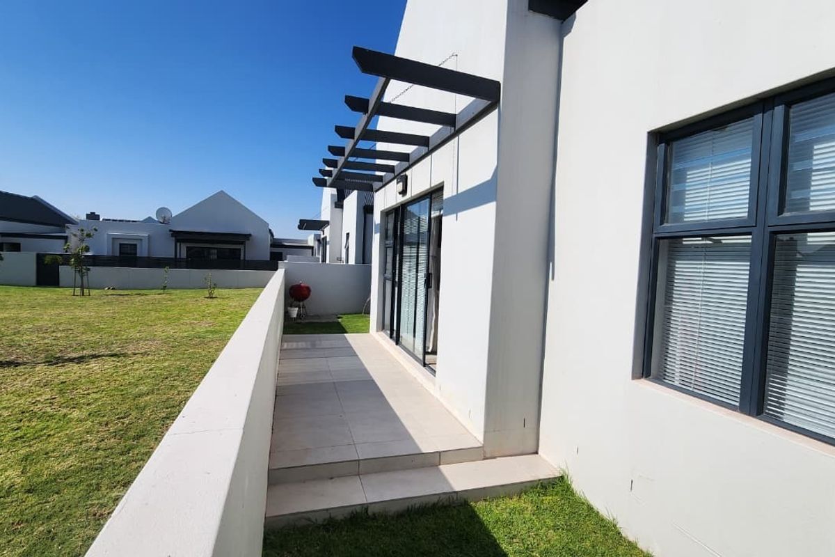 Rear view of the property featuring a tiled patio with a pergola, sliding glass doors, and a private garden area with boundary walls.