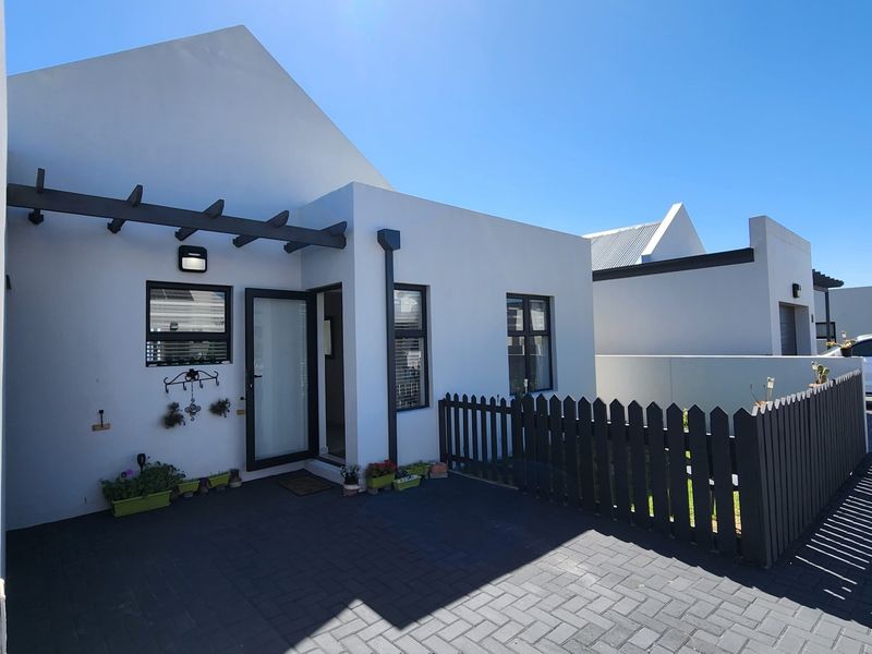 Front elevation of a modern residential property featuring a paved driveway, timber pergola, and a neat picket fence.