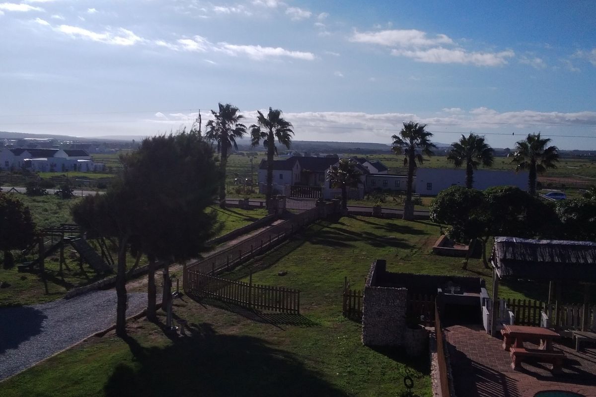 An elevated view of the small holding property, showcasing the expansive garden, paved driveway, and outdoor entertainment area with a thatched lapa.