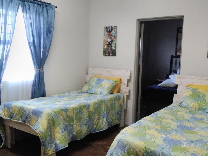 A functional bedroom featuring neutral walls, a window with curtains, and a doorway leading to an adjacent room.
