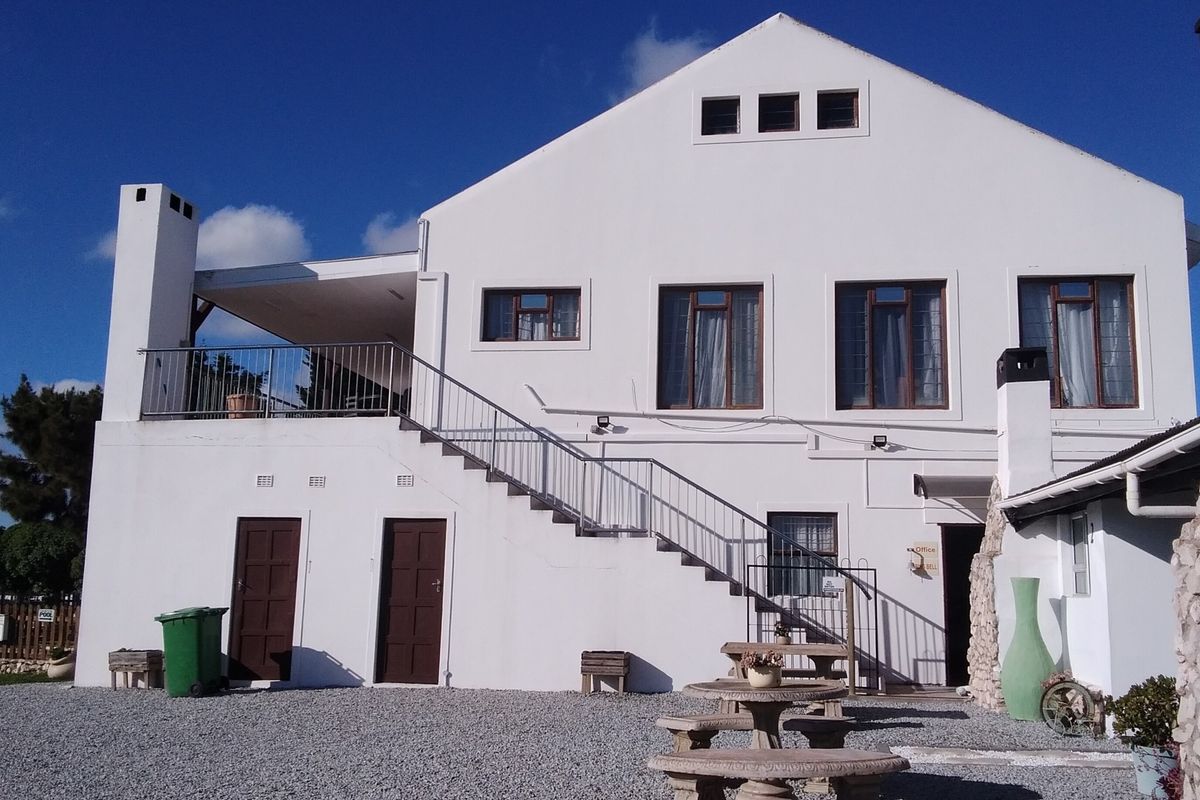 Rear elevation of a multi-level building featuring an external staircase leading to an upper balcony, stone masonry accents, and a gravel courtyard area.
