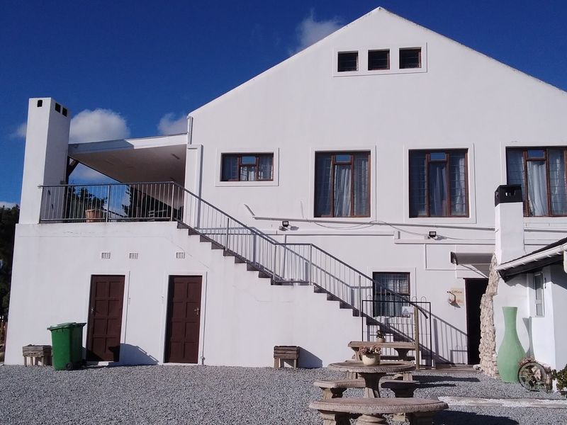 Rear elevation of a multi-level building featuring an external staircase leading to an upper balcony, stone masonry accents, and a gravel courtyard area.