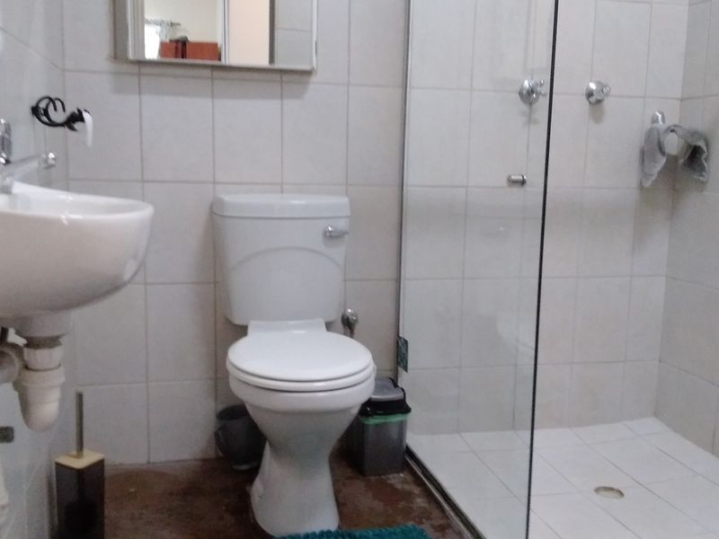 A functional bathroom featuring a pedestal basin, standard toilet, and a glass-enclosed shower with tiled finishes throughout.