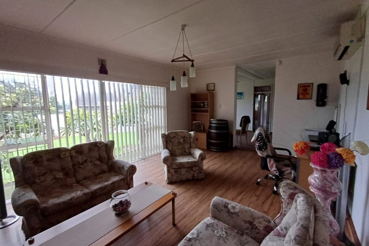 A spacious living room featuring laminate flooring, large windows with vertical blinds, and a wall-mounted air conditioning unit.