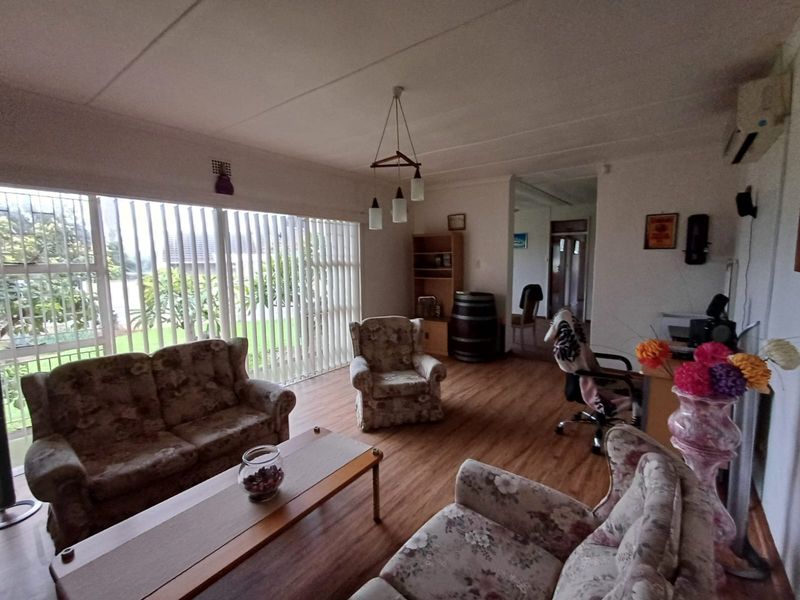 A spacious living room featuring laminate flooring, large windows with vertical blinds, and a wall-mounted air conditioning unit.