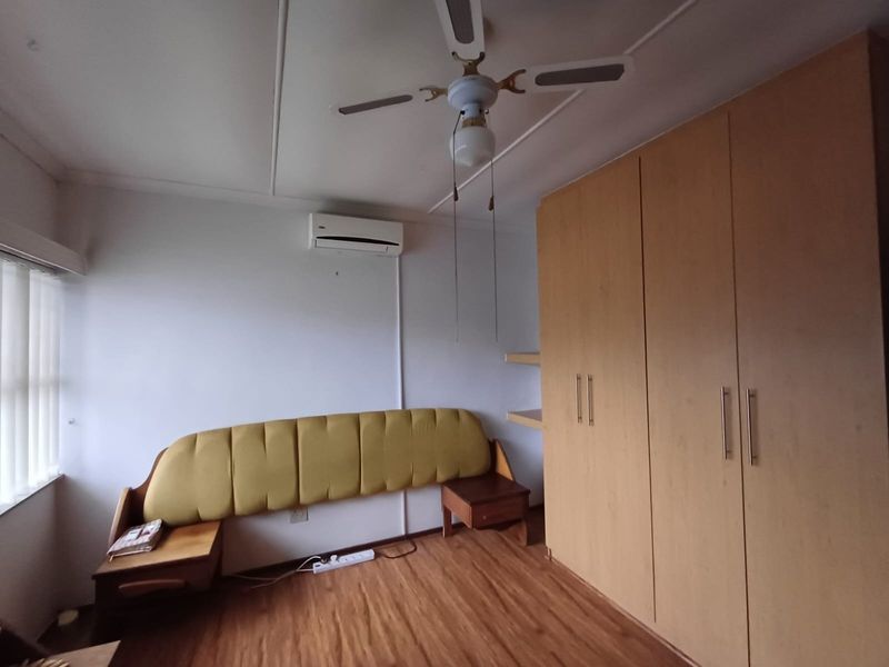 A bedroom featuring laminate flooring, a built-in wardrobe, a ceiling fan, and a wall-mounted split-system air conditioner.