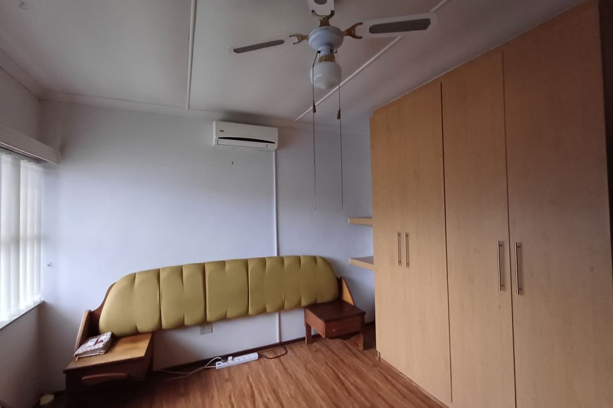 A bedroom featuring laminate flooring, a built-in wardrobe, a ceiling fan, and a wall-mounted split-system air conditioner.