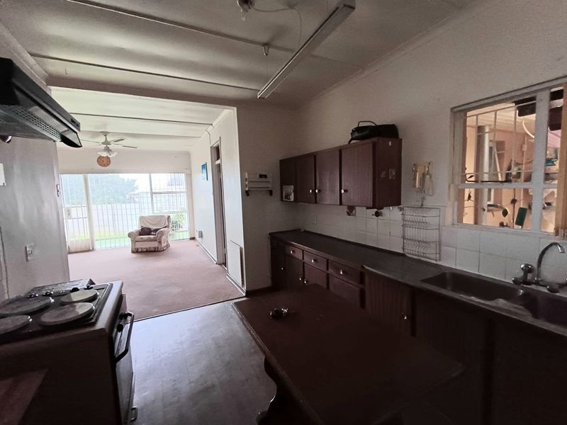 Open plan kitchen and living area featuring dated cabinetry, functional sink, and security bars on windows, offering potential for modernization and renovation.
